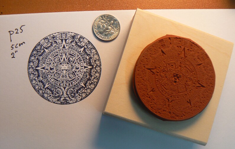 May include: A 2-inch diameter rubber stamp with a detailed design of the Aztec calendar. The stamp is mounted on a wooden block.