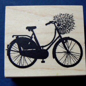 Könnte beinhalten: Eine schwarze Silhouette eines Fahrrads mit einem Blumenkorb am Lenker. Das Fahrrad befindet sich auf einem hölzernen Hintergrund.