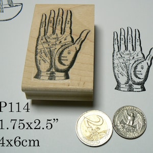May include: A wooden stamp with a black and white illustration of a hand with lines and symbols. The stamp is 1.75 inches by 2.5 inches and 4 centimeters by 6 centimeters. The text on the stamp reads "P114".