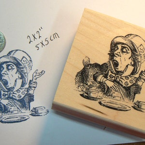 Puede incluir: Un sello de goma de madera con una ilustración en blanco y negro del Sombrerero Loco de Alicia en el País de las Maravillas. El Sombrerero Loco lleva un sombrero con la palabra "JUICY" en él. El sello mide 2 x 2 pulgadas o 5 x 5 cm.