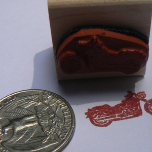 May include: A wooden mounted rubber stamp with a red motorcycle design. The stamp is approximately the size of a US quarter.