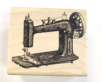May include: A vintage-style wooden stamp featuring a black and white illustration of a sewing machine with the text "New Companion" on the side.