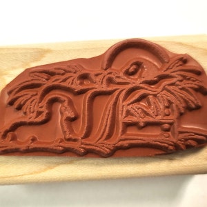 May include: A brown wooden mounted rubber stamp with a design of a manger scene with a star above the manger and palm trees on either side.