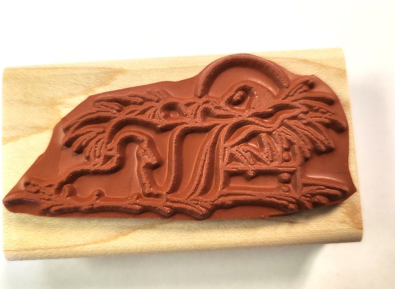 May include: A brown wooden mounted rubber stamp with a design of a manger scene with a star above the manger and palm trees on either side.