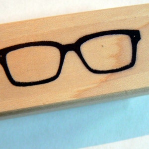 May include: A wooden block stamp with a black silhouette of eyeglasses.