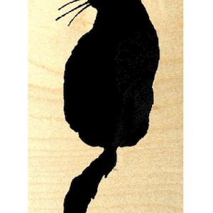 Puede incluir: Silueta negra de un gato sentado con la cola enroscada alrededor de su cuerpo. El gato está mirando hacia la derecha y hacia arriba. La silueta está sobre un fondo de madera marrón claro.