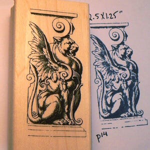 Op de afbeelding: Een houten stempel met een gedetailleerde illustratie van een gevleugelde griffioen. De stempel meet 6,35 x 3,18 cm en bevat een bijpassende inktindruk op papier. De griffioen is afgebeeld in een zittende pose met ingewikkelde vleugel- en lichaamsdetails.