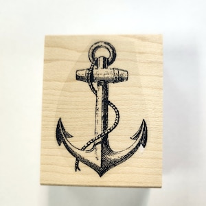 May include: A wooden stamp with a black and white illustration of an anchor with a rope wrapped around it.