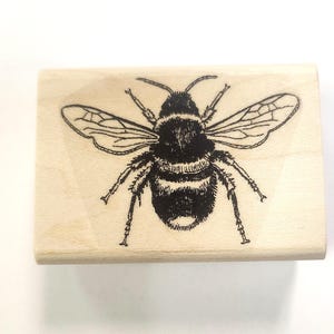Könnte beinhalten: Eine Schwarzweißillustration einer Biene auf einem Holzblock. Die Biene hat einen flauschigen Körper und Flügel.
