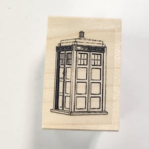 May include: A wooden stamp with a black and white illustration of a police box with the text "Police Box" on the side.