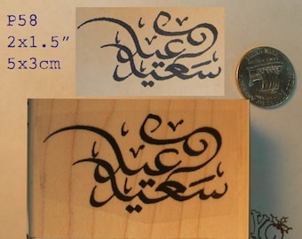 May include: A wooden stamp with the Arabic phrase "Eid Mubarak" in black ink. The stamp is 2 inches by 1.5 inches and measures 5 cm by 3 cm.