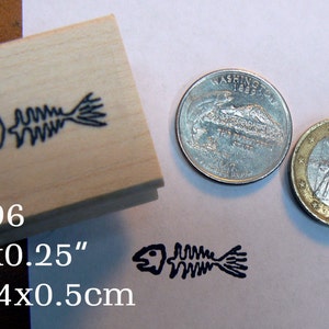 Könnte beinhalten: Ein Stempel aus Holz mit einem schwarzen Fischskelett-Design. Der Stempel misst 1 Zoll mal 0,25 Zoll oder 2,4 cm mal 0,5 cm. Der Stempel ist mit "P96" gekennzeichnet.