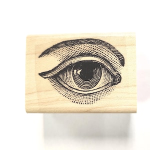 May include: A wooden rubber stamp with a black and white illustration of an eye.