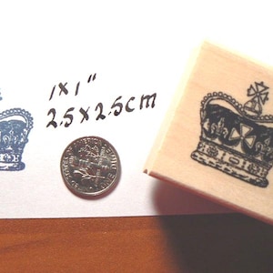May include: A wooden stamp featuring a detailed crown design, with a stamped impression and a coin for scale. The stamp is approximately 2.5 x 2.5 cm, and the stamped image is in blue ink.