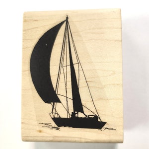 May include: A wooden mounted rubber stamp with a black silhouette of a sailboat with a sail.