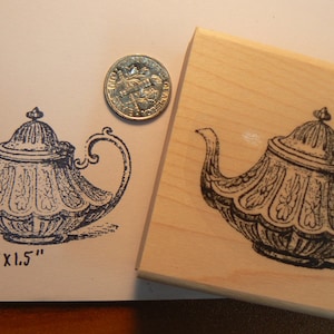 May include: A black and white image of a teapot with a decorative design. The teapot is 2.25 inches by 1.5 inches. The image is printed on a wooden block.