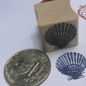 May include: A wooden rubber stamp with a black and white image of a seashell. The stamp is about the size of a quarter.