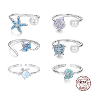 Può includere: Set di sei anelli d'argento con accenti di perle e disegni in smalto blu. I disegni includono una stella marina, una conchiglia, una tartaruga, una manta, una conchiglia con una perla e una stella marina con una perla.