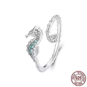 Può includere: Anello d'argento con un design a cavalluccio marino e pietre preziose blu. L'anello è regolabile e ha una fascia attorcigliata.