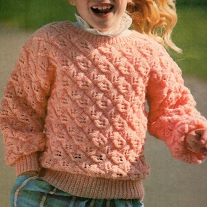 May include: A coral-pink knitted jumper featuring a textured diamond pattern. The jumper has long sleeves and a ribbed hem and cuffs. A white lace-trimmed collar is visible. This classic style is suitable for cooler weather, offering warmth and comfort.