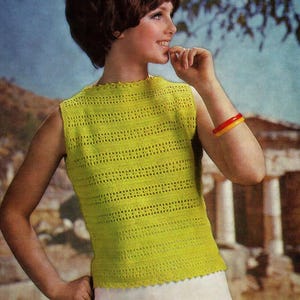 Puede incluir: Un top sin mangas de ganchillo color chartreuse con rayas caladas horizontales. El top tiene un escote y dobladillo festoneados. Se lleva un brazalete rojo y amarillo en el brazo. El fondo presenta una escena borrosa al aire libre.