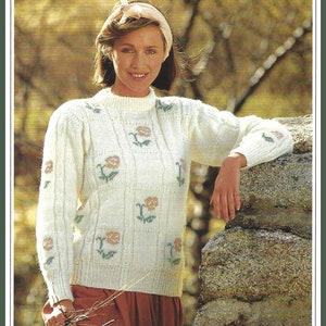 Op de afbeelding: Een witte gebreide trui met een bloemenpatroon. De trui heeft een ronde hals en lange mouwen. De bloemen zijn in tinten roze, groen en wit.