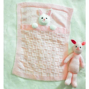 May include: A pink knitted baby blanket with a white bunny peeking out from the top. A pink crocheted bunny toy is on the right side of the blanket.