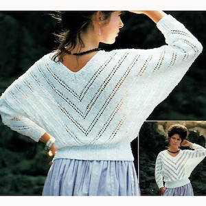 May include: A white, V-neck sweater with a chevron design. The sweater has long sleeves and a loose fit. The model is wearing a light purple skirt. The sweater is made of a knitted material.