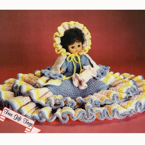 May include: A vintage crochet doll with a blue dress, a yellow bonnet, and a ruffled skirt. The doll is holding a pink item. The skirt has yellow, white, and blue stripes. The image includes a banner that says "Free Gift Tags".