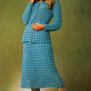 May include: A vintage, light blue crochet skirt suit. The suit includes a long-sleeved, button-down jacket and a knee-length skirt. The outfit is paired with white fishnet stockings and white heels. The crochet pattern is visible throughout the suit.