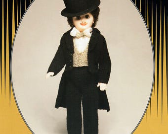 May include: A vintage doll dressed in a black suit, top hat, and bow tie. The doll has a painted mustache and is wearing a knitted vest. The doll is standing in front of an oval frame with a gold and black design.