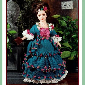 Könnte beinhalten: Eine Porzellanpuppe in einem teeblauen Kleid mit rosa und weißen Akzenten. Das Kleid ist mit gehäkelten Rosen und Spitze verziert. Die Puppe hat braunes Haar und trägt eine Perlenkette.