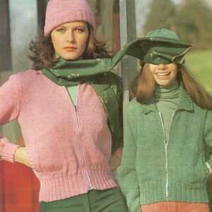 May include: Two women wearing knitted sweaters and hats. The woman on the left is wearing a pink sweater with a green scarf and a pink hat. The woman on the right is wearing a green sweater with a green hat and a green scarf.