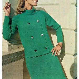 May include: A vibrant green knit two-piece outfit. The ensemble includes a long-sleeved jacket with large, decorative buttons and a matching skirt. The jacket has a high collar and a wrap-style design. The outfit is made of a textured knit fabric.