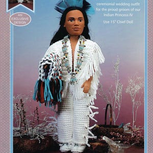 May include: A doll wearing a white crochet ceremonial wedding outfit, with a beaded necklace and a blue feathered headdress. The outfit includes a fringed shawl and pants with white ties. The text reads "An Exclusive Design".