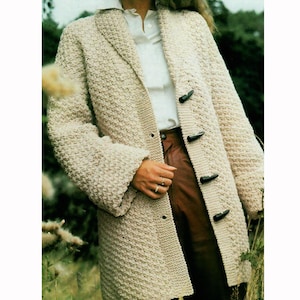 May include: A beige, textured knit coat with a notched collar and toggle closures. The long coat features a tailored design and is worn over a white shirt and brown pants. The coat has a classic, timeless style.