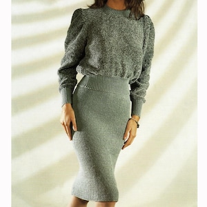 May include: A two-piece gray knit set featuring a long-sleeved sweater with puffed shoulders and a ribbed pencil skirt. The set is made of a textured knit fabric and has a fitted silhouette. The sweater has a crew neck and ribbed cuffs.