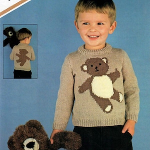 May include: A beige knitted jumper with a brown teddy bear design on the front. The jumper has a crew neck and long sleeves. The teddy bear has a white tummy and brown paws.
