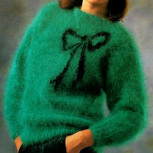 Könnte beinhalten: Ein grüner, flauschiger Pullover mit einem schwarzen Schleifendesign auf der Vorderseite.