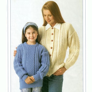 May include: A woman and a girl wearing knitted sweaters. The woman's sweater is cream with a cable knit pattern and buttons down the front. The girl's sweater is blue with a textured pattern.