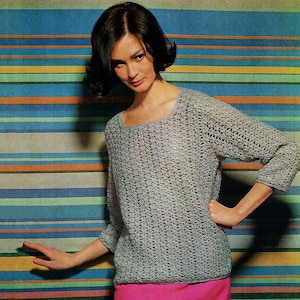 May include: A light gray, open-weave crochet sweater with three-quarter sleeves. The sweater has a scoop neckline and is paired with a bright pink skirt. The background features horizontal stripes in various colors, including blue, green, orange, and yellow.