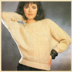 May include: A cream-colored knitted sweater with a round neckline and long sleeves. The sweater has a loose fit and is made of a soft, fuzzy yarn.