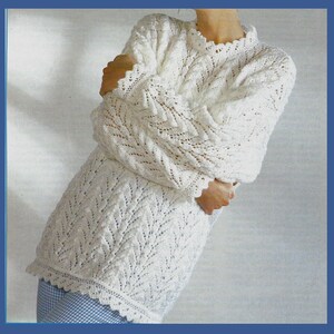 Könnte beinhalten: Weißer Häkelpullover mit einem zarten Spitzenmuster. Der Pullover hat einen runden Ausschnitt und lange Ärmel.