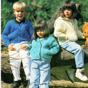 May include: Three children wearing knitted cardigans. The child on the left is wearing a blue cardigan, the child in the middle is wearing a turquoise cardigan, and the child on the right is wearing a cream cardigan.