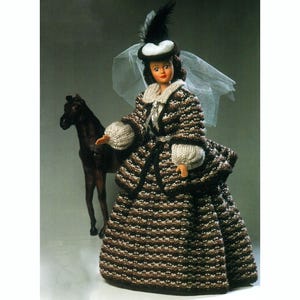 Puede incluir: Una muñeca vestida con un vestido a rayas marrones y blancas con un sombrero blanco y velo. La muñeca sostiene un pequeño caballo marrón.