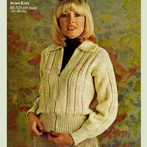 Op de afbeelding: Een crèmekleurige Aran-gebreide cardigan met een ritssluiting. De cardigan heeft een kabelbreipatroon en een kraag. De cardigan wordt getoond op een model met een borstomvang van 81-101 cm.