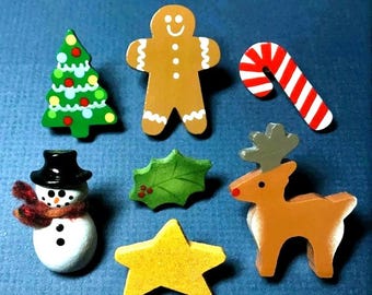 May include: A collection of wooden Christmas-themed ornaments. Includes a green Christmas tree, gingerbread man, candy cane, snowman, holly leaf, yellow star, and a reindeer. Each ornament is painted with bright colors and has a festive design.