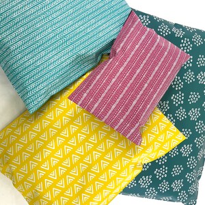 May include: Four fabric swatches with different geometric patterns. The swatches are teal with white chevron, pink with white stripes, yellow with white zigzags, and teal with white polka dots.