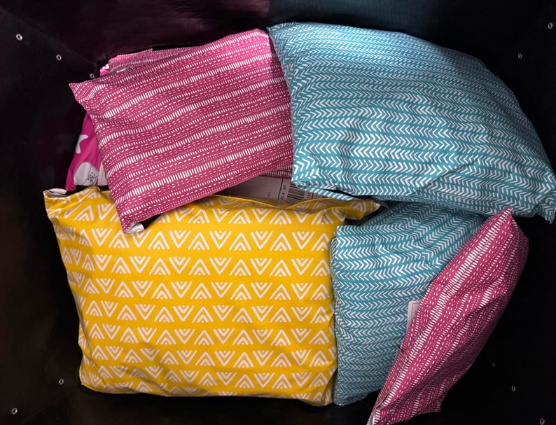 May include: A collection of five patterned pillowcases in a black tote bag. The pillowcases are in various colours and patterns, including yellow with white triangles, teal with white chevron, and pink with white stripes.