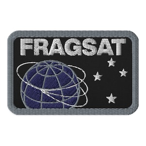 Może przedstawiać: Naszywka haftowana w kolorze czarnym i szarym z napisem "FRAGSAT" w kolorze białym. Naszywka przedstawia niebieską kulę ziemską z białymi liniami i białymi pierścieniami wokół niej. W tle znajdują się cztery białe gwiazdy.